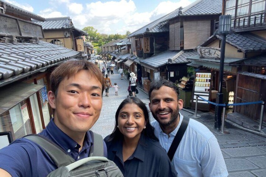 Una calle con edificios tradicionales, una persona tomándose un selfie y otra persona al fondo. 5