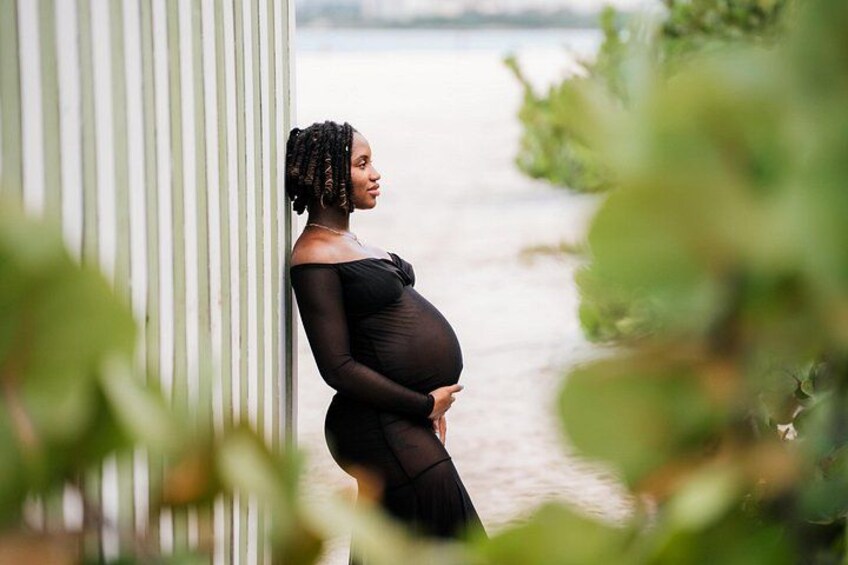 A pregnant woman standing by a railing with a body of water in the background. 2