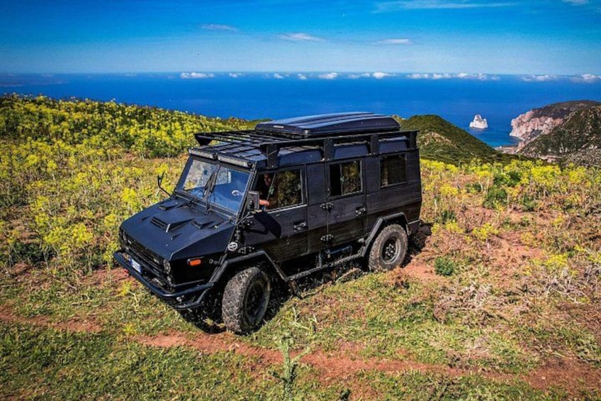 A black off-road vehicle parked on a grassy hillside with a coastal view in the background. 1
