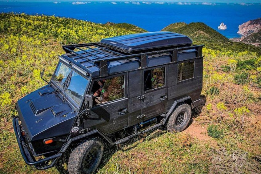 A black off-road vehicle with a roof rack on a grassy hillside with a view of the ocean. 5