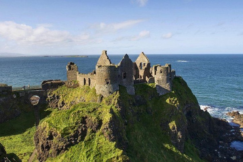 A historic stone castle on a grassy cliff overlooking the sea. 4
