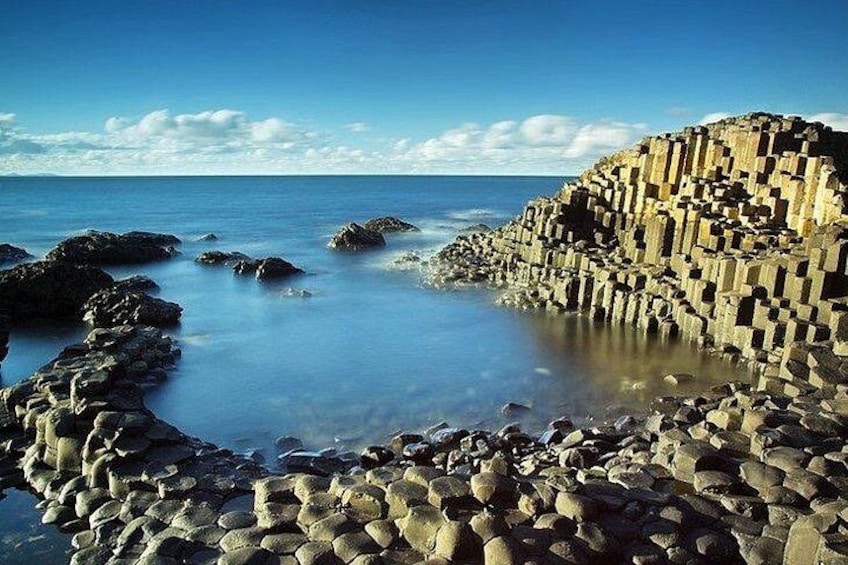 A coastal landscape with a rocky shoreline, clear blue water, and a distant horizon. 1