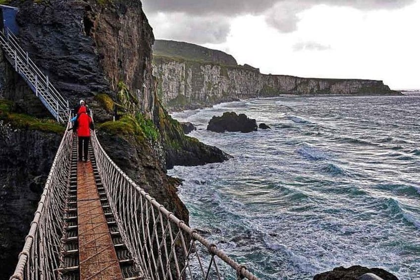 A person walking on a rope bridge over a cliff, with the ocean below. 2