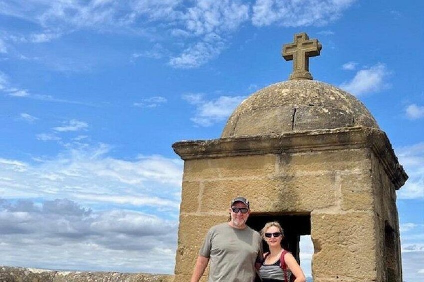 Una edificación de piedra con una cruz en la parte superior, cielo azul despejado y algunas nubes. 3