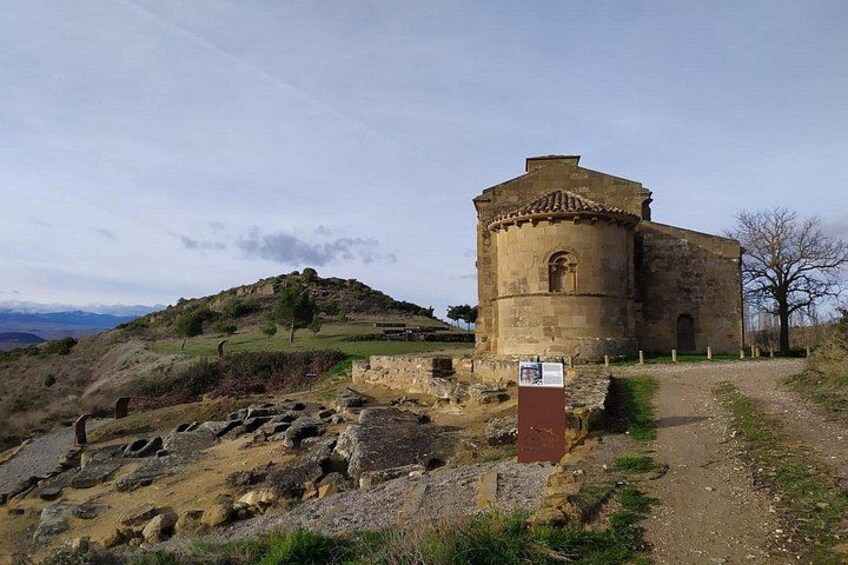 Un edificio histórico de piedra con una torre circular, rodeado por un sendero de grava y vegetación escasa. 4