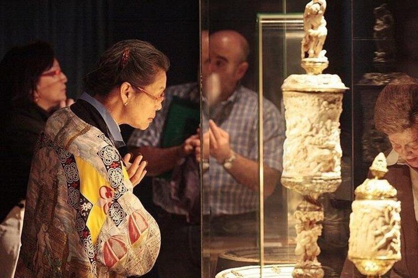 Una persona observa una exhibición de artefactos antiguos, incluyendo un objeto alto y cilíndrico con figuras en la parte superior. 1