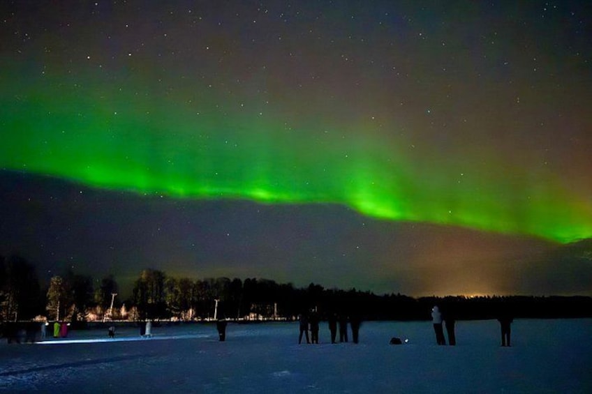 The Northern Lights over a frozen landscape with people observing. 5