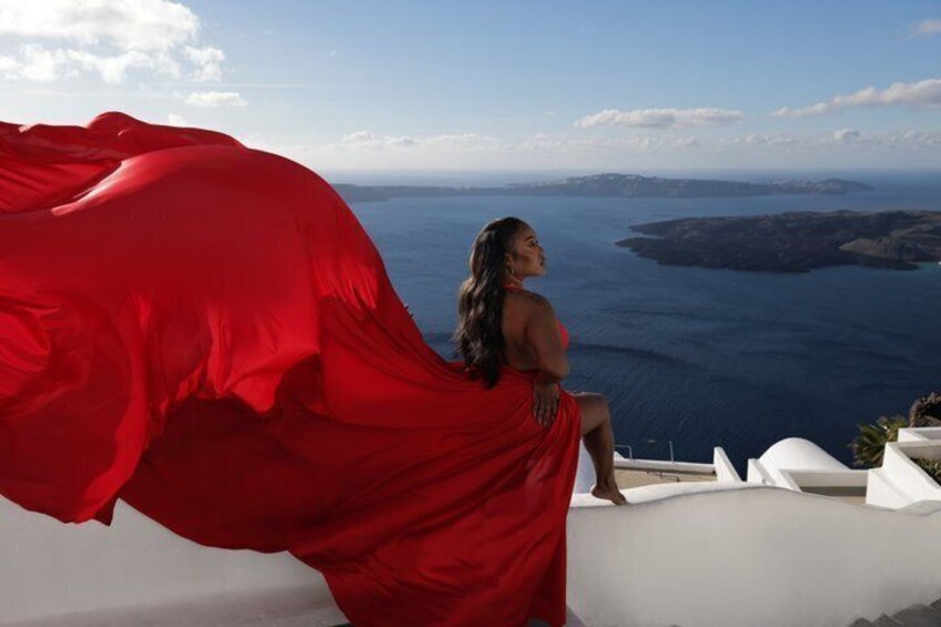 A person in a red dress sitting on a white balcony overlooking a coastal landscape. 1