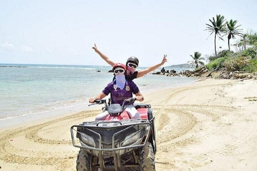 A person on a quad bike on a sandy beach with palm trees in the background. 1