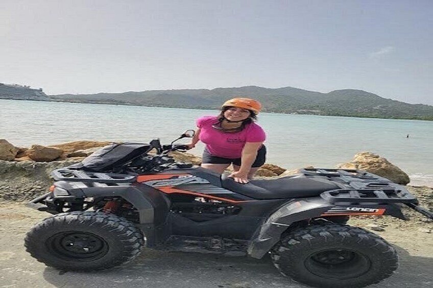 Una persona sentada en un vehículo todo terreno cerca de un cuerpo de agua con montañas al fondo. 2