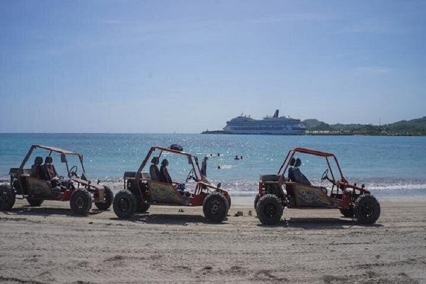 Tres vehículos todoterreno estacionados en una playa arenosa, con un crucero al fondo. 5