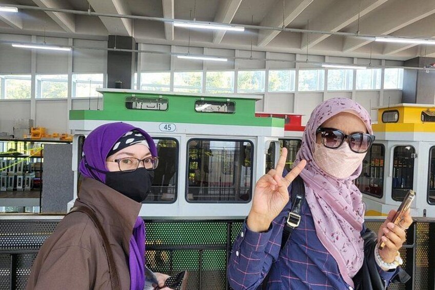 Two people at a train station, one holding a phone and the other making a peace sign. 2