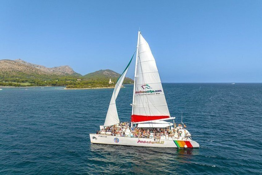 A sailboat with a white hull and red and green stripes on the bow, sailing on a calm sea with a mountainous coastline in the background. 2