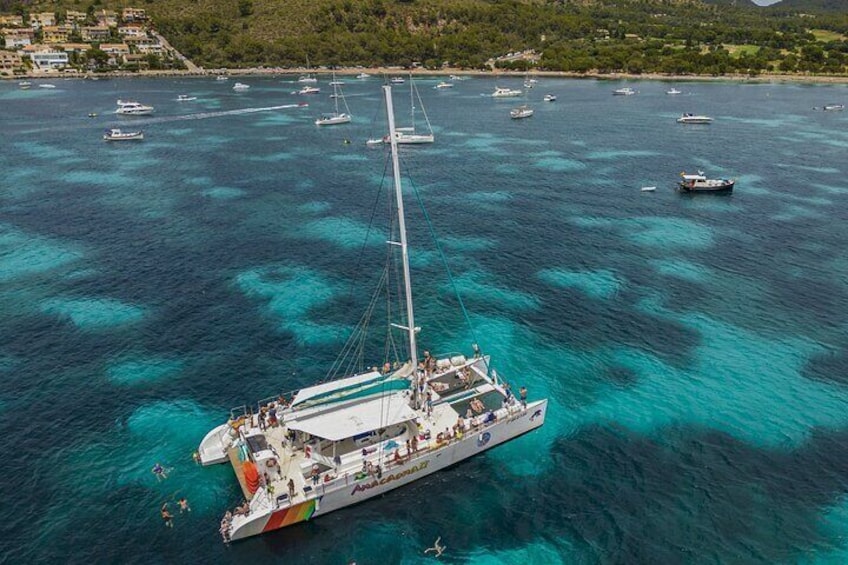 Un velero con pasajeros en un mar turquesa de aguas cristalinas y embarcaciones al fondo. 1