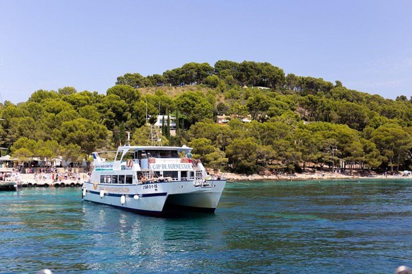 A boat named 'Cap de Formentor' on calm waters with a forested hill in the background. 4