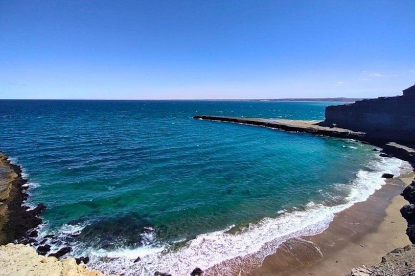 A coastal landscape with clear blue waters, a sandy beach, and rocky cliffs. 3