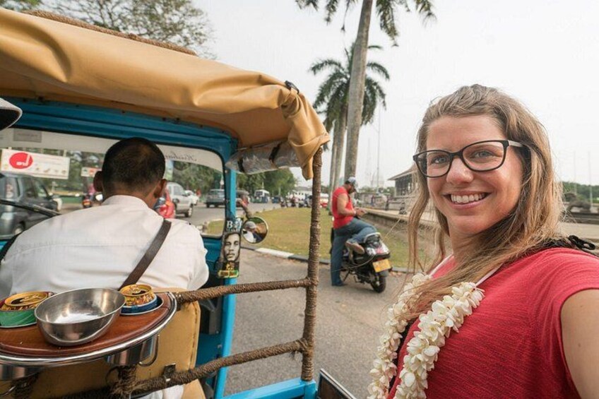 A tuk-tuk with a passenger, a man driving, and a motorbike in the background. 2