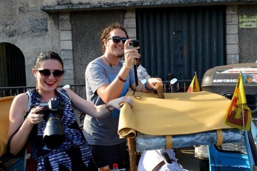 Two people taking photographs with cameras, a table with a yellow cloth, and a vehicle with flags. 2