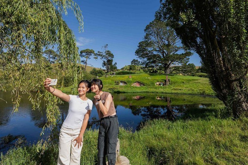 Two people taking a selfie by a pond with trees and grass in the background. 3