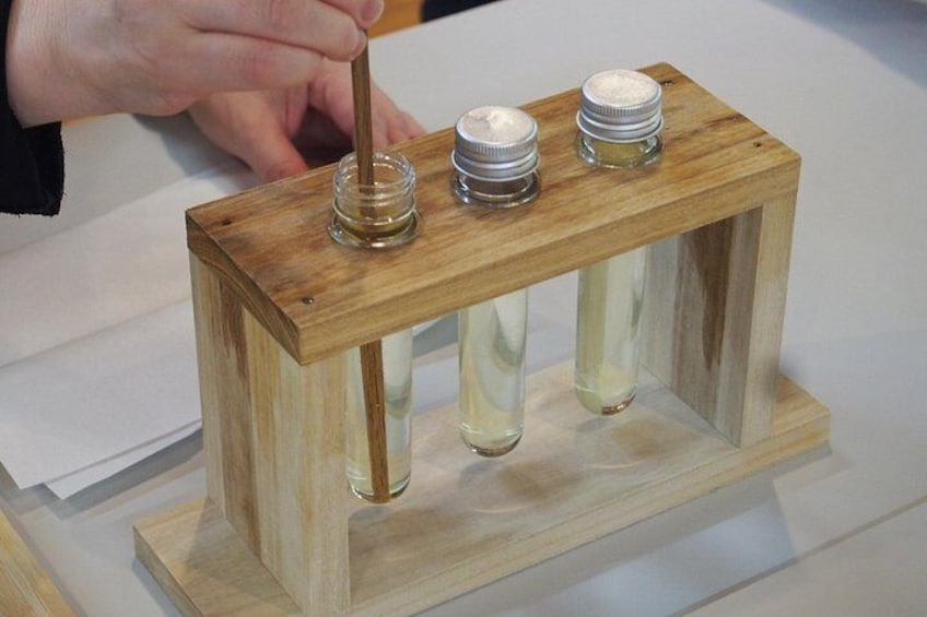 Ein hölzerner Stand mit drei Glasflaschen und einer Hand, die einen Stock hält. 5
