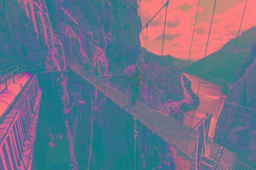 A suspension bridge with metal railings, a rocky gorge, and a river below. 2