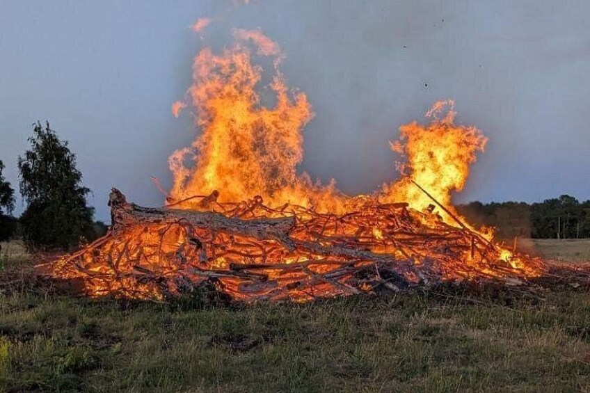 A large fire burning in an open field with trees in the background. 2