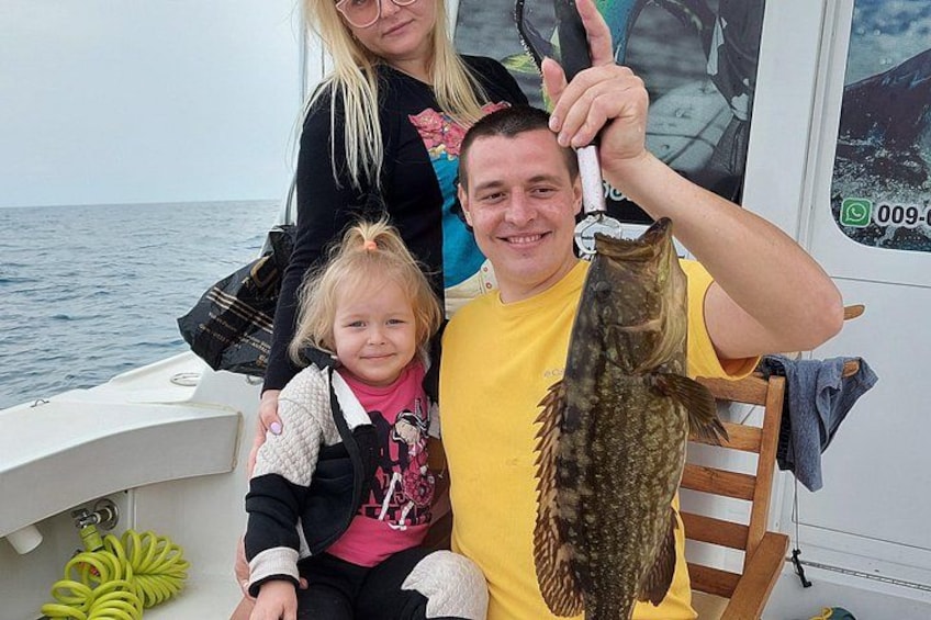 A person holding a fish on a boat with a child and another person. 3