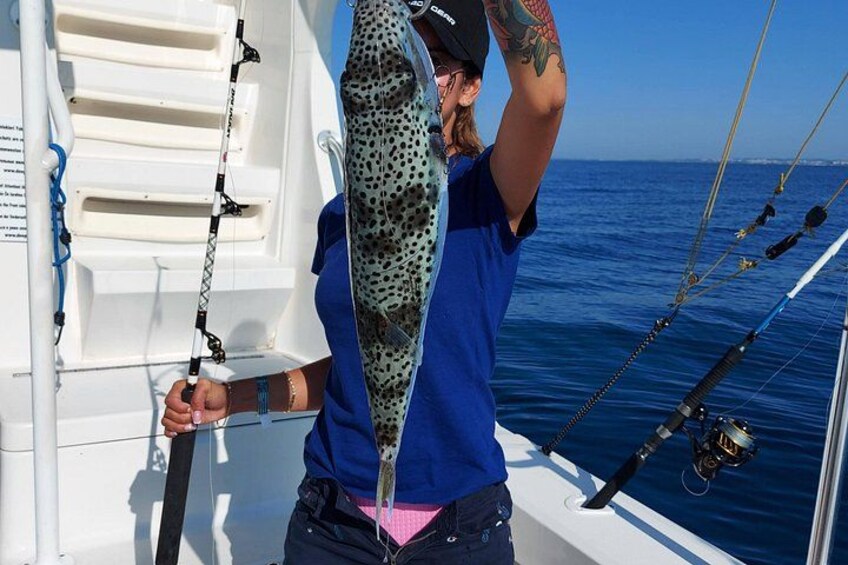 A person holding a large fish on a boat with fishing rods and a clear blue sky in the background. 4