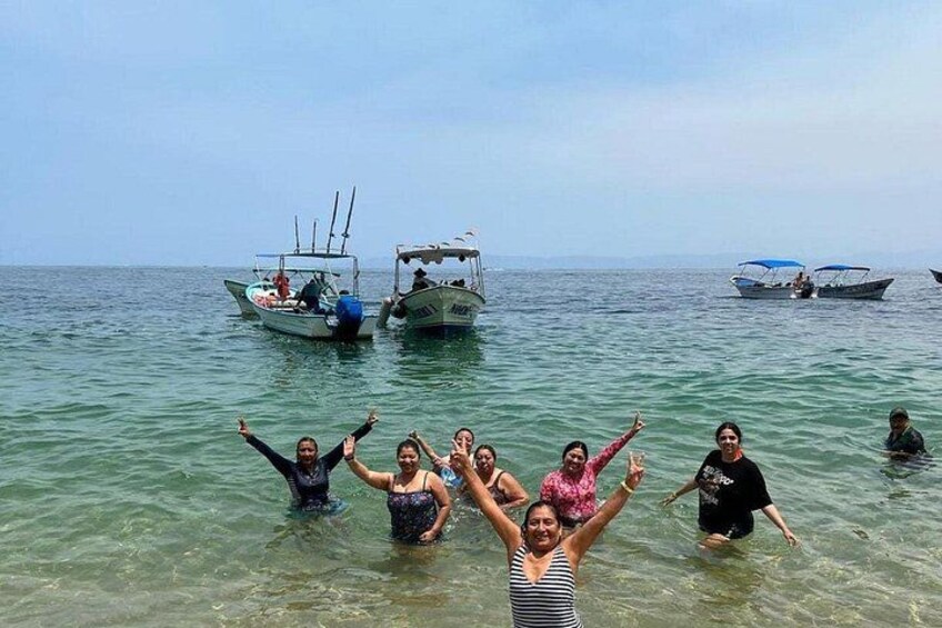 A group of people in shallow water with boats in the background. 1