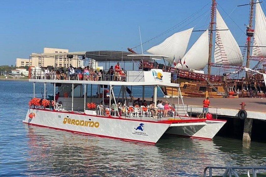 A boat named 'geronimo' docked at a pier with people on board and a sailboat in the background. 4