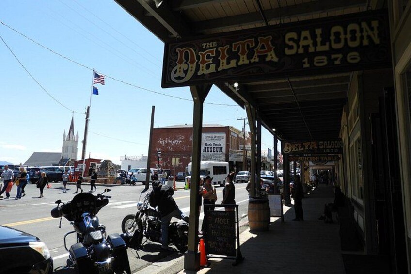 A street scene with a building labeled 'Delta Saloon 1876' and a church steeple in the background. 3