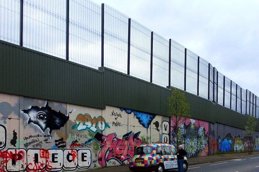A building with graffiti art on its side, a fenced area above, and a colorful car parked in front. 2