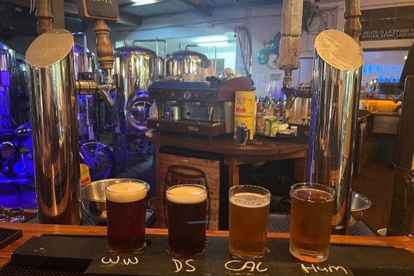 Un bar con tres vasos de cerveza frente a grifos etiquetados como 'Ww', 'DS', 'CAC' y 'Hym'. 2