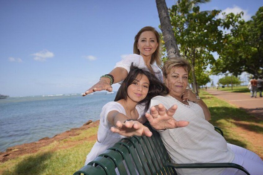 Tres personas sentadas en un banco junto al agua, con cielo despejado y árboles al fondo. 5
