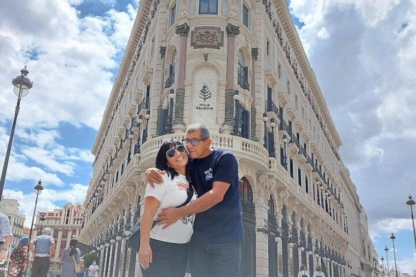 A couple embracing in front of a historic building with ornate architecture. 2
