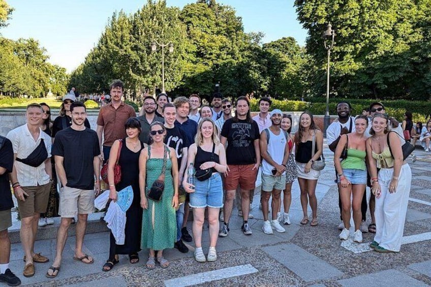A group of people standing on a paved area with trees and a lamppost in the background. 4