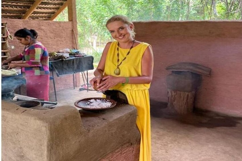 Eine Person in einem gelben Kleid kocht im Freien, mit einem Backofen aus Ziegeln und einer weiteren Person im Hintergrund. 3