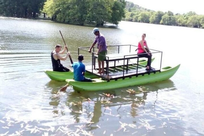 Eine Gruppe von Menschen in einem grünen Boot mit Geländer rudert auf einem ruhigen See, der von Bäumen umgeben ist. 5