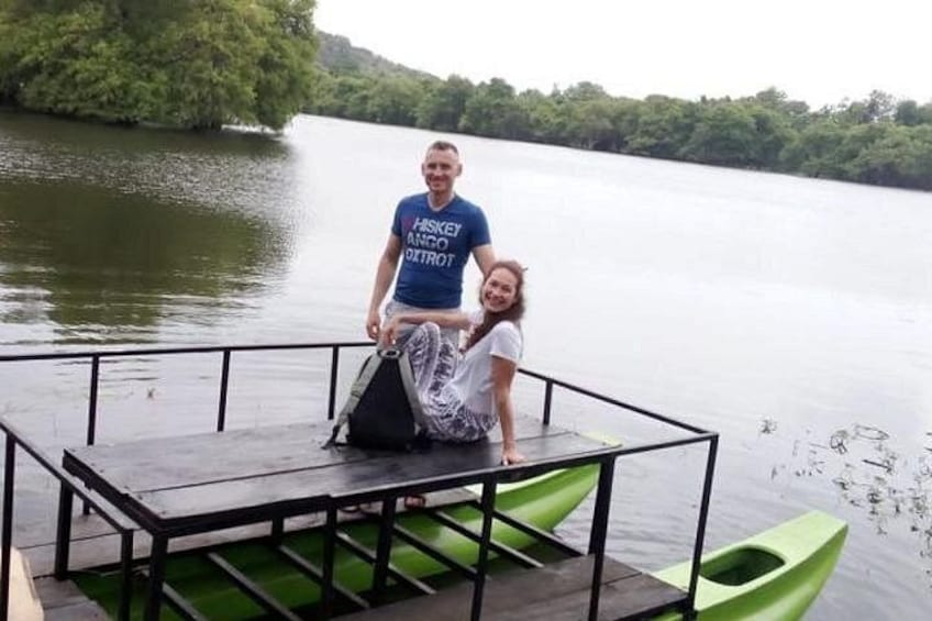 Eine Person sitzt auf einer Anlegestelle, ein grünes Kajak daneben, eine andere Person steht, und im Hintergrund liegt ein ruhiger See. 4