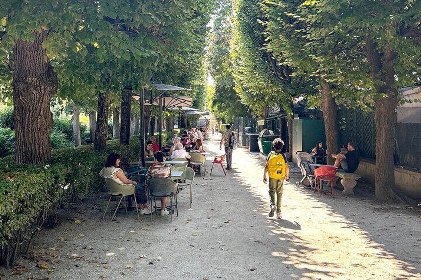 A tree-lined outdoor café with people dining and walking. 3