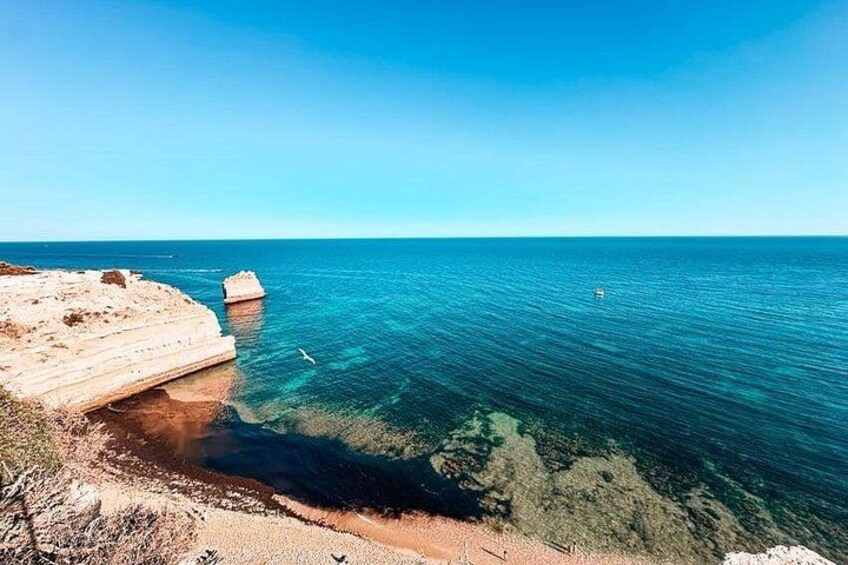 Paesaggio costiero con acque blu cristalline, una spiaggia sabbiosa e un promontorio roccioso. 2