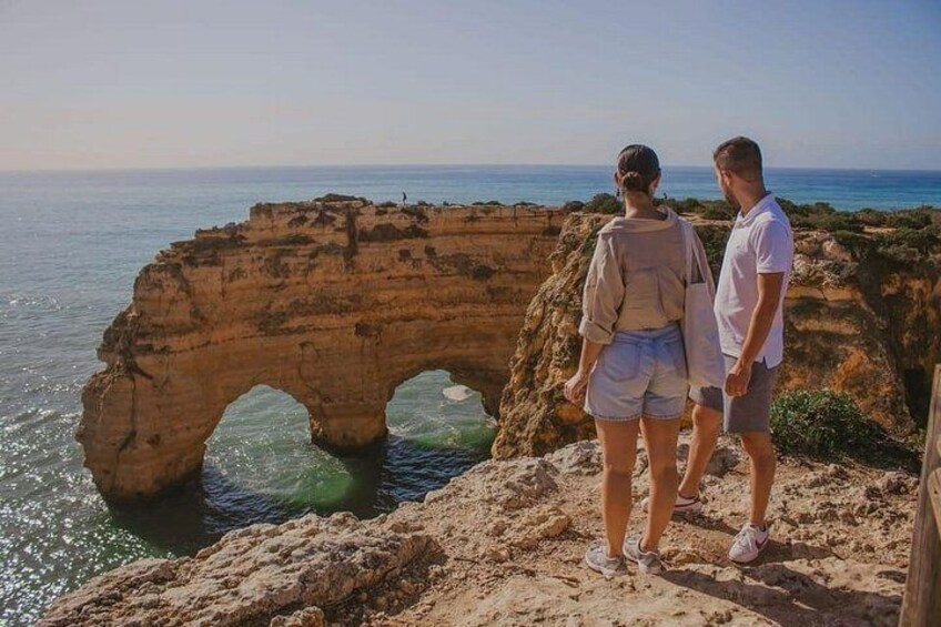 Una coppia in piedi su uno sperone roccioso con vista su un arco naturale. 5