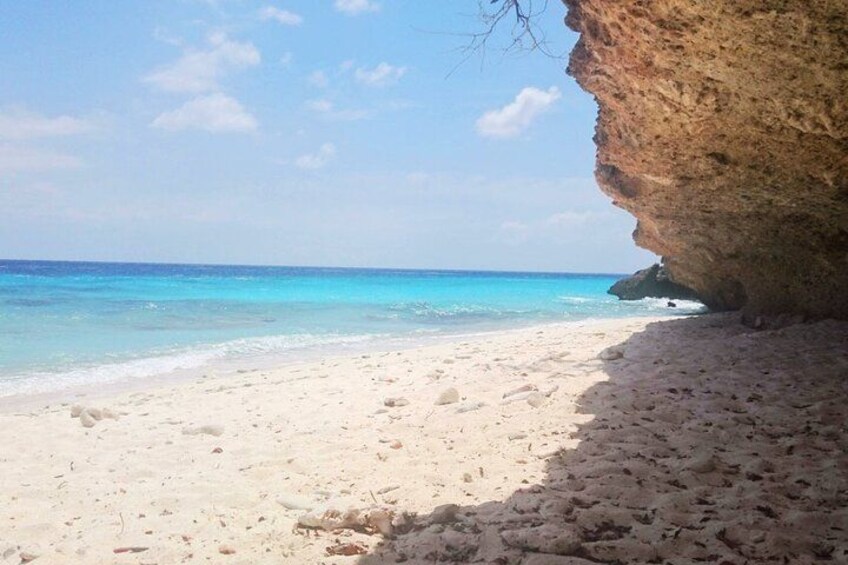 A beach with clear turquoise water, white sand, and a large rock formation. 1