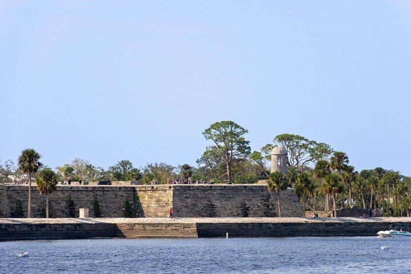 A stone fortification with a lighthouse, palm trees, and a calm sea. 3