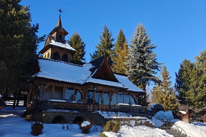 Een houten kerk met een hoge toren en een met sneeuw bedekte dak, omgeven door altijdgroene bomen. 3