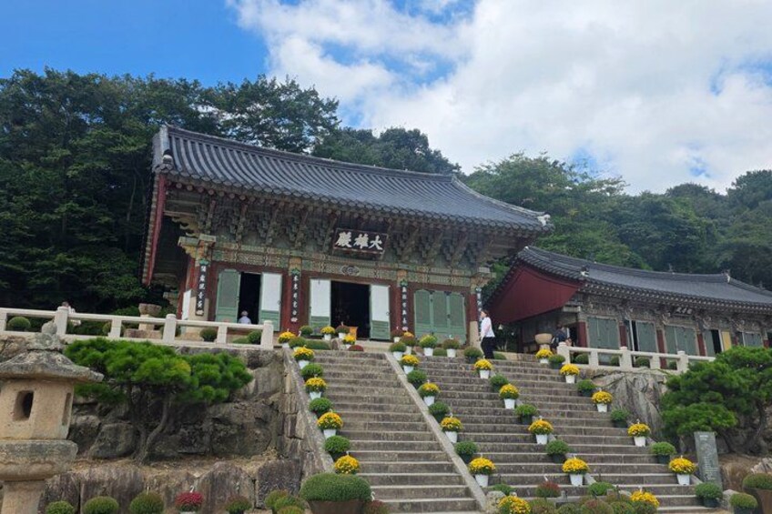Een traditionele Koreaanse tempel met een trap die naar de ingang leidt, omringd door groen en stenen trappen. 3