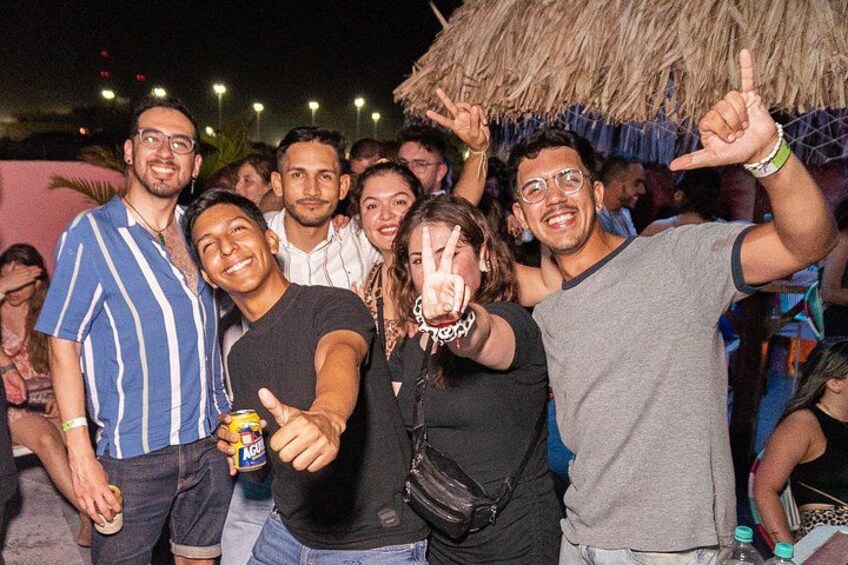 Un gruppo di persone a un evento all'aperto, con una struttura in paglia sullo sfondo. 1