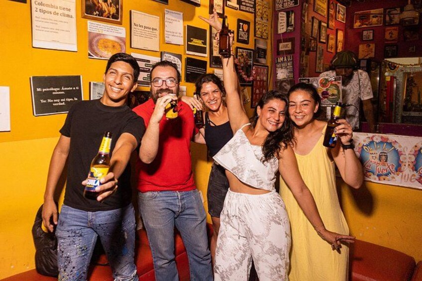 A group of people holding bottles, standing in front of a wall with various posters and text. 2