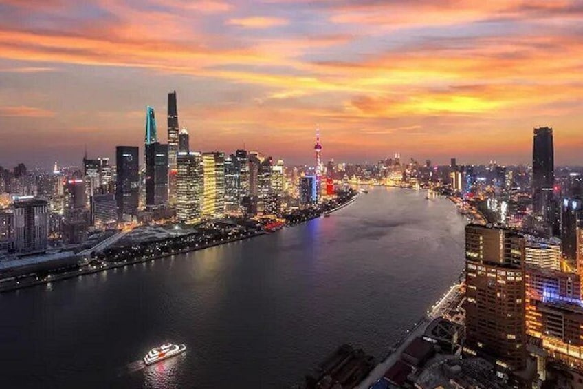 A city skyline at dusk with illuminated buildings, a river, and a boat on the water. 3
