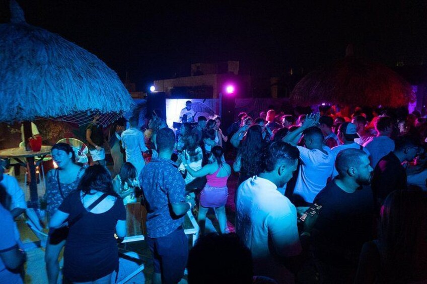En livlig udendørs begivenhed med dansende mennesker og en scene med en DJ. 3